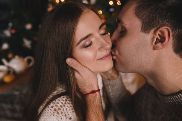 Couple on the bed in the bedroom. Dark interior. New Year's and Christmas. Hugs and kisses. Love. White sweater and high socks. Romantic meeting. A date lovers. - Фото, изображение