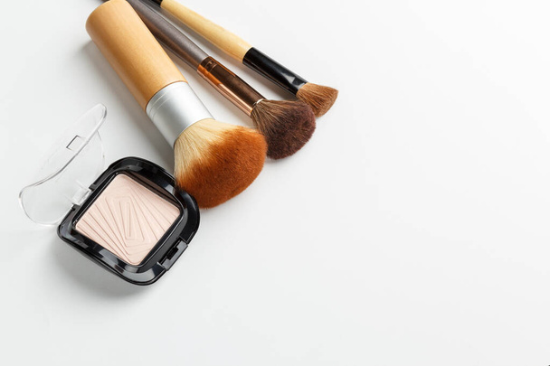 Cepillos de maquillaje de diferentes tamaños y polvo de maquillaje sobre un fondo blanco. Vista superior
. - Foto, imagen