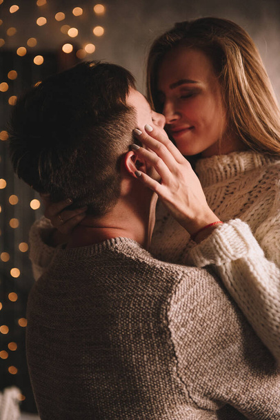 Couple on the bed in the bedroom. Dark interior. New Year's and Christmas. Hugs and kisses. Love. White sweater and high socks. Romantic meeting. A date lovers. - Fotografie, Obrázek