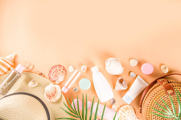 Summer cosmetics background. Summer skincare, sunscreen cosmetics, travel kit miniatures flat lay. Trendy peach background, with women bag, sea shells, tropical leaves, straw hat. Copy space above  - Photo, Image