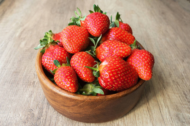 Nahaufnahme Bild von leckeren leckeren großen roten Erdbeeren liegen in runden Holzteller auf hellem Holzhintergrund, antioxidative Ernährung, gesundes Ernährungskonzept - Foto, Bild