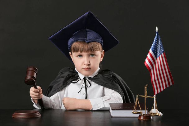 Портрет маленького судьи, сидящего за столом на темном фоне
 - Фото, изображение
