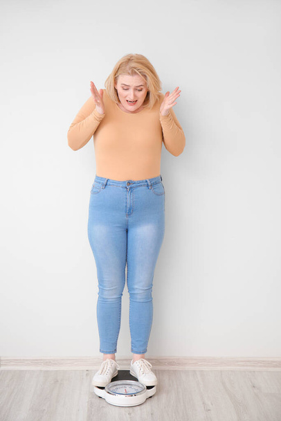 Kłopotliwa kobieta z nadwagą, z wagą przy białej ścianie. Koncepcja odchudzania - Zdjęcie, obraz