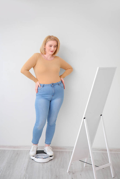 Mujer con sobrepeso con escamas cerca del espejo. Concepto de pérdida de peso
 - Foto, Imagen