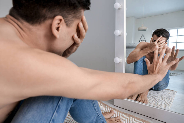 Homem descontente com anorexia perto do espelho em casa
 - Foto, Imagem