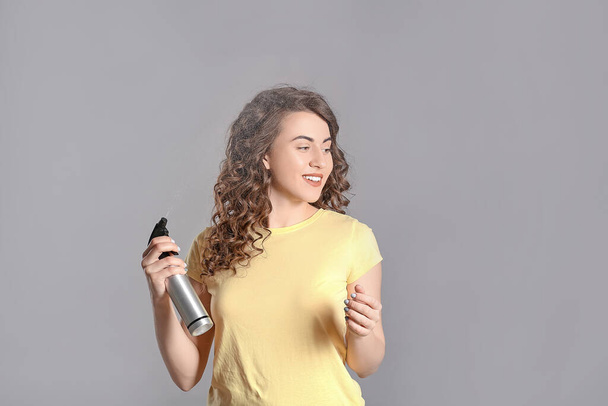 Beautiful young woman with hair spray on grey background - Zdjęcie, obraz