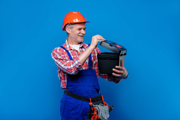 Photo of professional plumber  and builder in blue uniform open his  toolbox  isolated on blue background. - Foto, Imagem