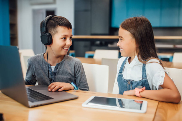 Due piccoli amici felici, ragazzo e ragazza che utilizzano tablet digitale intelligente per giocare nella moderna stanza blu
. - Foto, immagini