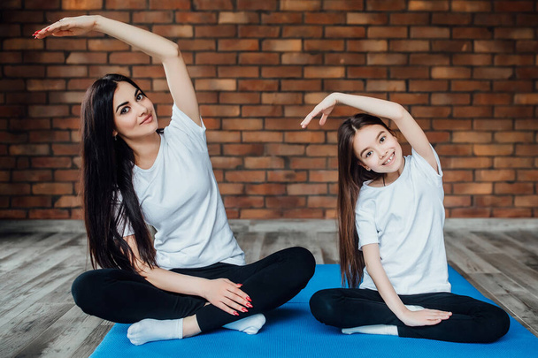 Two pretty sisters  wearing in sport wear holding hands on had and doing meditation. - Foto, Imagem