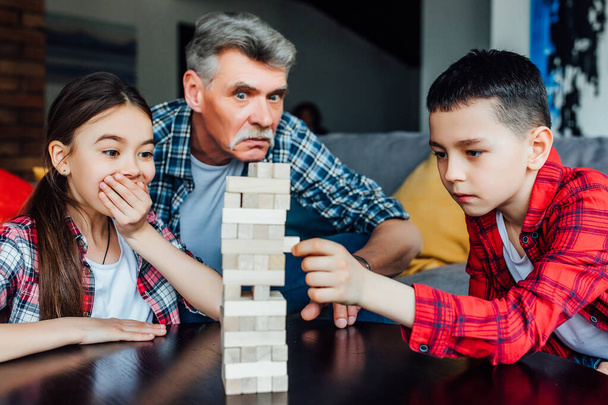 Funny grandfather playing blocks wood tower game with daughter and son. - Φωτογραφία, εικόνα