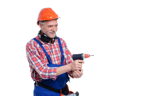 Πορτρέτο του ηλικιωμένου άνδρα, επαγγελματίας εργαζόμενος σε μπλε στολή με ηλεκτρικό τρυπάνι απομονώνονται σε λευκό φόντο. - Φωτογραφία, εικόνα