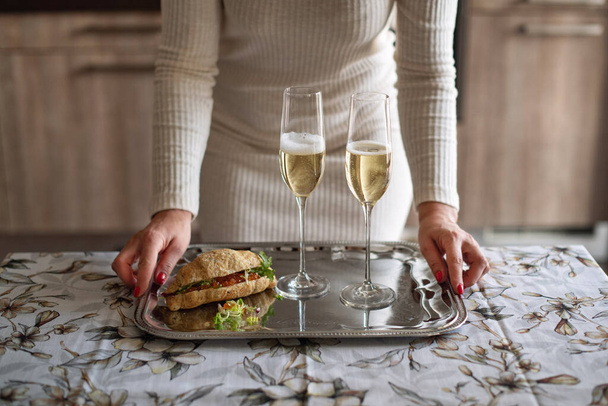 Girl in a beige dress with glasses of champagne. Home romantic evening during quarantine. Elegant modern party with a glass of sparkling wine. - Photo, Image