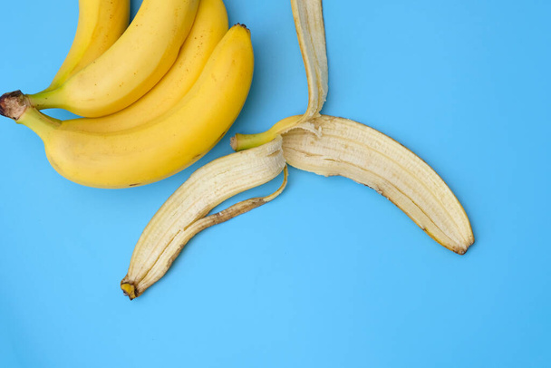 青い背景にバナナの皮とバナナの束。バナナを食べることの利点,食事.バナナの上からの皮. - 写真・画像