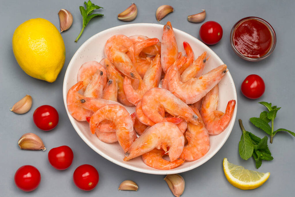 Frozen shrimp and ice in white bowl. Rice noodles, lemon, mint garlic, tomato sauce. Healthy nutrition. Gray background. Flat lay - Foto, afbeelding