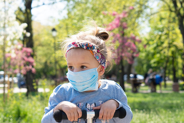 Карантин, вірус, коронавірус, KOVID - 19, епідемія, поняття грипу. Маленька дівчинка в захисній масці біля квітучого дерева. Алергія - Фото, зображення