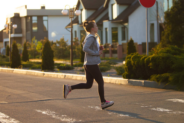 Young female runner, athlete is jogging in the city street in sunshine. Beautiful caucasian woman training, listening to music - Φωτογραφία, εικόνα