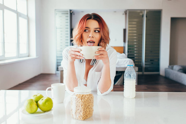 atrakcyjna dziewczyna lizanie płatków kukurydzianych z mlekiem na śniadanie podczas kwarantanny - Zdjęcie, obraz