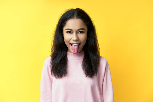 Pretty black woman showing tongue and looking at the camera on yellow background - Foto, Imagen