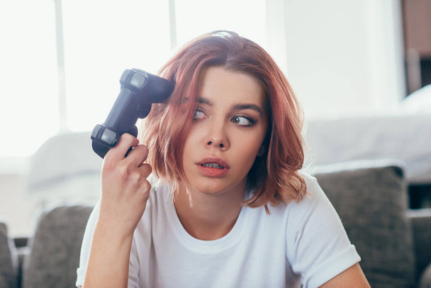 KYIV, UKRAINE - APRIL 15, 2020: thoughtful girl playing video game with joystick at home on self isolation - Фото, зображення