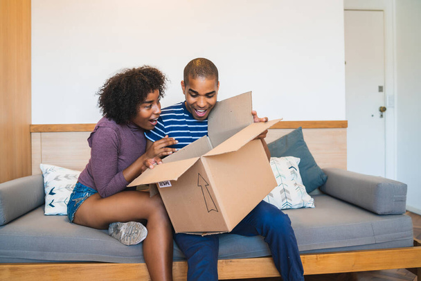 Portrait of happy young latin couple opening a package at home. Delivery, shipping and postal service concept. Buy online and stay at home. Covid-19 Quarantine. - Foto, Imagen