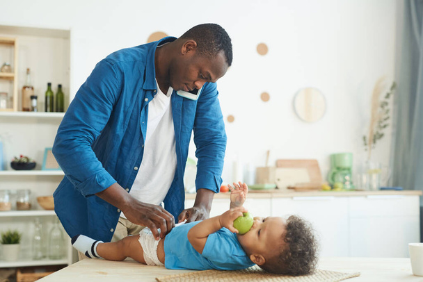 Vue de côté portrait d'homme mûr afro-américain appelant femme tout en changeant la couche pour bébé à l'intérieur de la maison, espace de copie
 - Photo, image