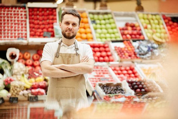 Pas nahoru portrét vousatého muže v zástěře stojící u stánku s ovocem a zeleninou na farmářském trhu a dívající se do kamery, kopírovací prostor - Fotografie, Obrázek