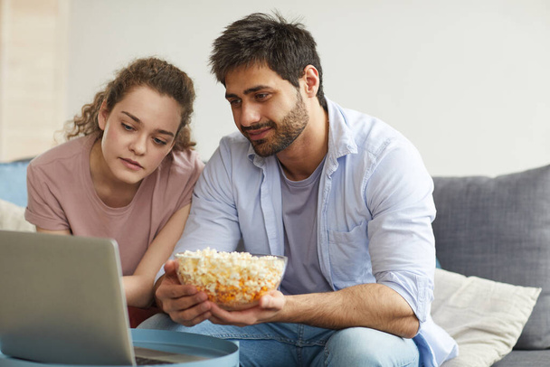 Portret van een modern jong stel dat online films kijkt via een laptop en een grote kom popcorn vasthoudt, kopieer ruimte - Foto, afbeelding