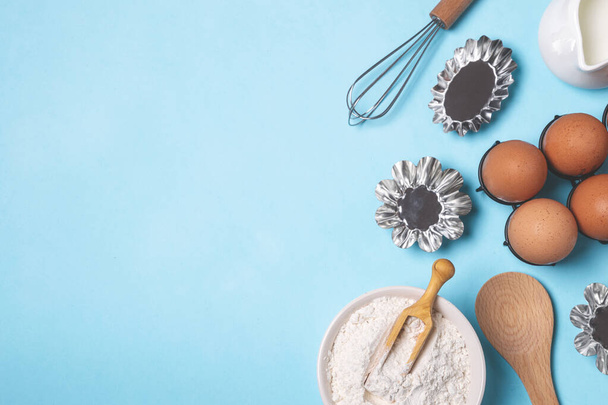 Baking pastry background, ingredients, kitchen utensils, eggs, whisk, flour on light blue background, flat lay, copy space - Photo, Image