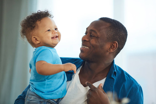 Retrato de papá afroamericano feliz jugando con el niño blanco risueño sentado en la mesa de la cocina, espacio para copiar
 - Foto, Imagen