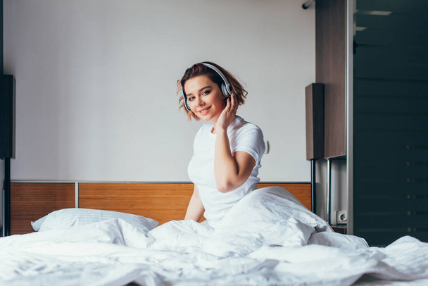 smiling girl listening music with headphones in bed during quarantine - Foto, immagini