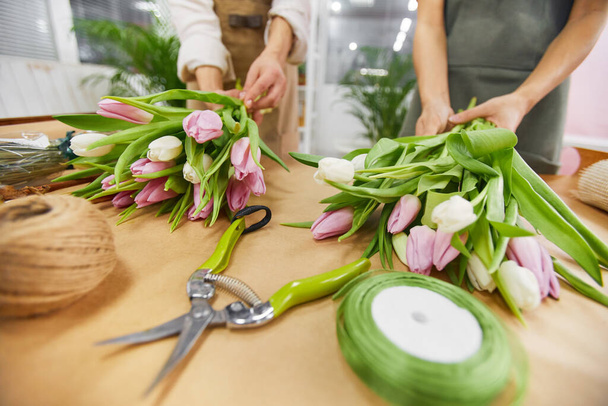 Çiçekçide çalışırken bahar sezonu için lale buketleri ve çiçek kompozisyonları düzenleyen tanınmamış iki genç kadına yakın durun. - Fotoğraf, Görsel