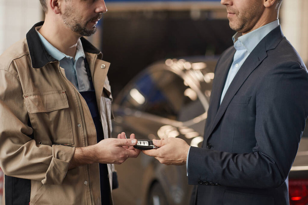 Mekaanikon keskiosa, joka antaa auton avaimet liikemiehelle tarkistettuaan ylellisen auton vuotuisessa tarkastuksessa autokorjaamossa, kopiotila - Valokuva, kuva
