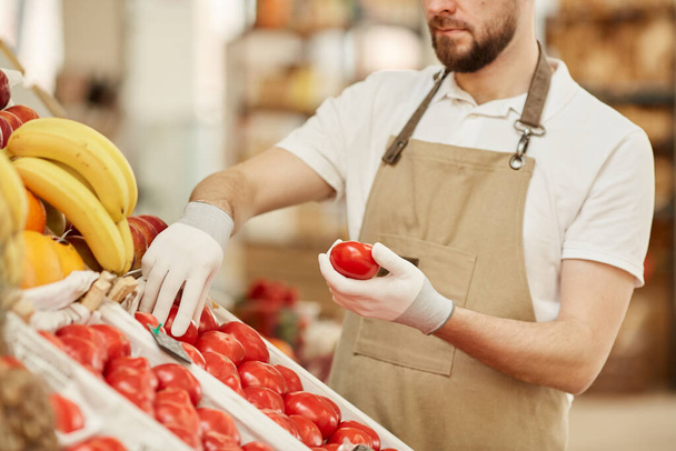 Portrait recadré d'un homme barbu tenant des tomates biologiques fraîches tout en vendant des produits locaux sur un stand de fruits et légumes dans un marché fermier, espace pour copier
 - Photo, image