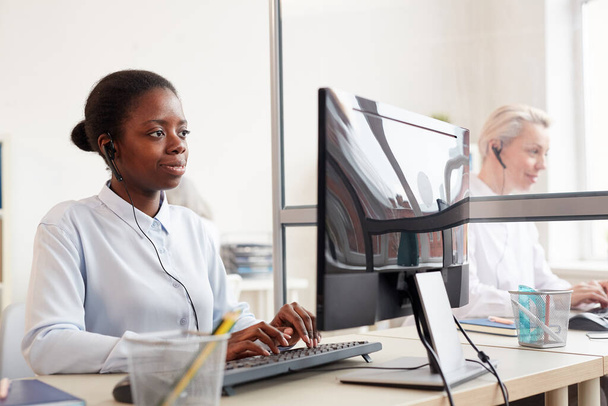 職場でコンピュータを使用している女性コールセンター事業者のグループは、前景にヘッドセットを身に着けている若いアフリカ系アメリカ人女性に焦点を当て、スペースをコピー - 写真・画像