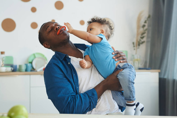 Retrato de feliz padre afroamericano jugando con su hijo pequeño mientras está sentado en el interior de la cocina, espacio para copiar
 - Foto, imagen