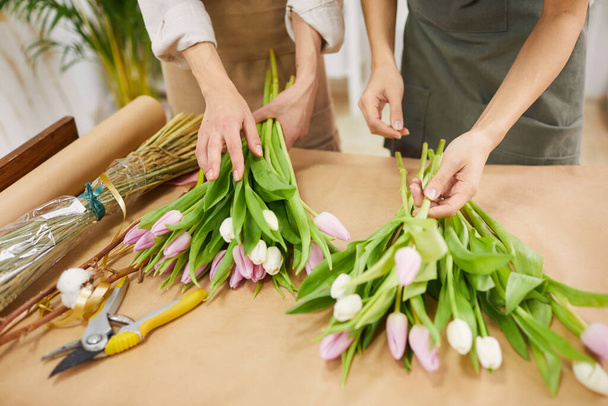 Vista de ángulo alto en dos mujeres jóvenes irreconocibles que arreglan ramos de tulipanes y composiciones florales para la temporada de primavera mientras trabajan en la florería, espacio para copiar
 - Foto, Imagen