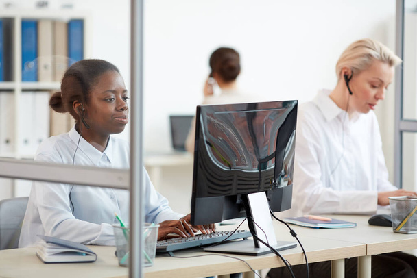 Groupe multi-ethnique de femmes opérateurs de centres d'appels utilisant des ordinateurs sur le lieu de travail, se concentrer sur les jeunes femmes afro-américaines portant un casque au premier plan, espace de copie
 - Photo, image
