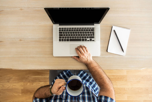 homem irreconhecível teletrabalho em casa com seu laptop, notebook e uma xícara de café, beber café, vista superior
 - Foto, Imagem