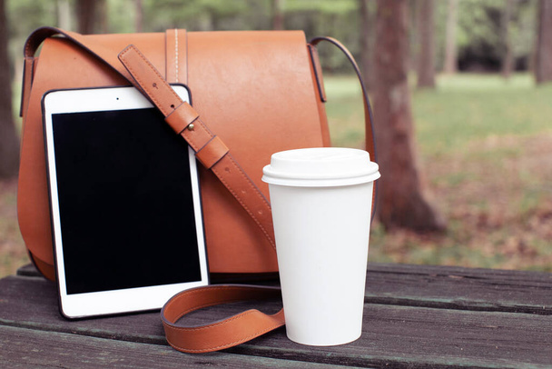 Stylowa damska torba, filiżanka kawy (herbata) i iPad na drewnianym stole w parku. Koncepcja stylu życia - Zdjęcie, obraz