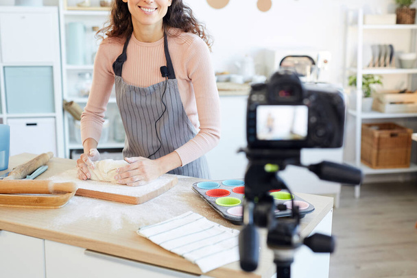Jeune femme adulte pétrissant la pâte pour les cupcakes tout en filmant la vidéo pour son blog alimentaire
 - Photo, image