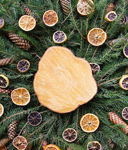 Dřevěný plátek na zelených větvích jedle zdobený sušenými plátky pomeranče a šiškami. Vánoční a novoroční ročník vinobraní zimní dovolená slavnostní složení. - Fotografie, Obrázek