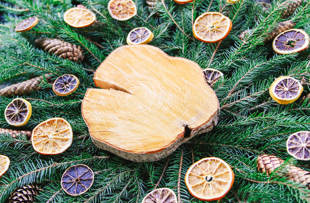 Ξύλινη φέτα σε πράσινα κλαδιά ελάτης διακοσμημένη με φέτες πορτοκαλιού και κώνους. Χριστούγεννα και Πρωτοχρονιά vintage χειμερινές διακοπές εορταστική σύνθεση. - Φωτογραφία, εικόνα