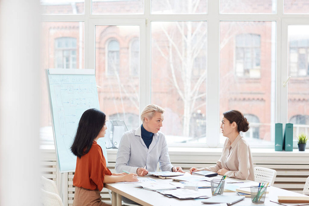 Группа современных бизнесвумен обсуждает проект, сидя за столом у окна во время встречи в конференц-зале, копировальное пространство
 - Фото, изображение
