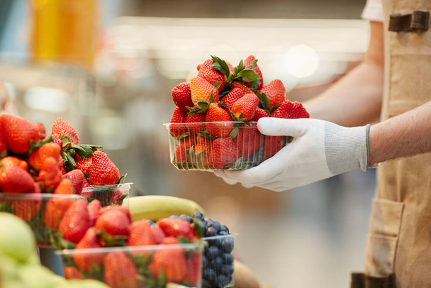Vue de côté gros plan de l'homme méconnaissable tenant boîte de délicieuses fraises fraîches au stand de fruits et légumes dans le marché des agriculteurs, espace de copie
 - Photo, image