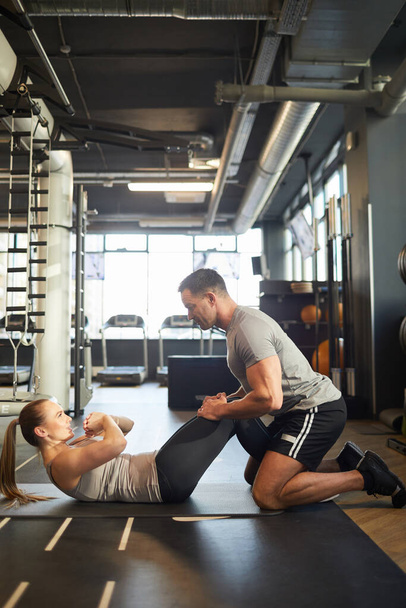 Visão lateral de ângulo largo no treinamento treinador muscular jovem mulher fazendo scrunches no ginásio, espaço de cópia - Foto, Imagem