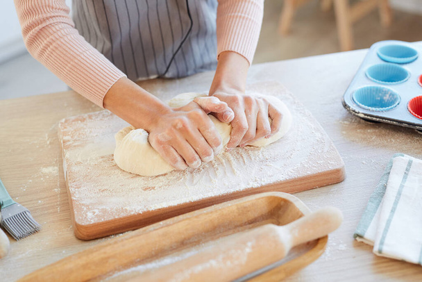 Tiro horizontal de alto ângulo de mãos femininas amassando a massa de padaria na placa de cozinha de madeira para cupcakes
 - Foto, Imagem