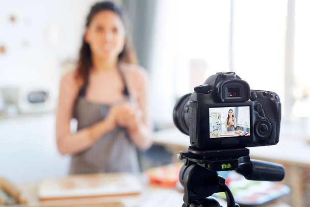 Mujer joven parada sola en su cocina disparando tutorial de panadería para su canal de blog de alimentos
 - Foto, imagen