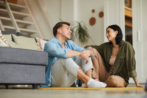 Ritratto di giovane coppia moderna che parla sinceramente mentre si siede sul pavimento in un accogliente interno domestico, copiare lo spazio - Foto, immagini