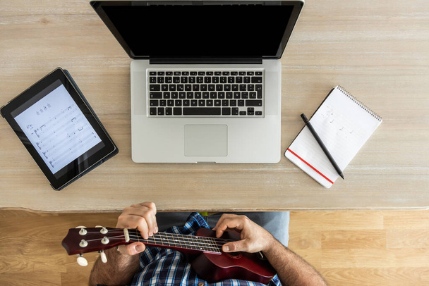 nerozpoznatelný muž nacvičující si ukulele doma s notebookem a tabletem, pohled shora - Fotografie, Obrázek