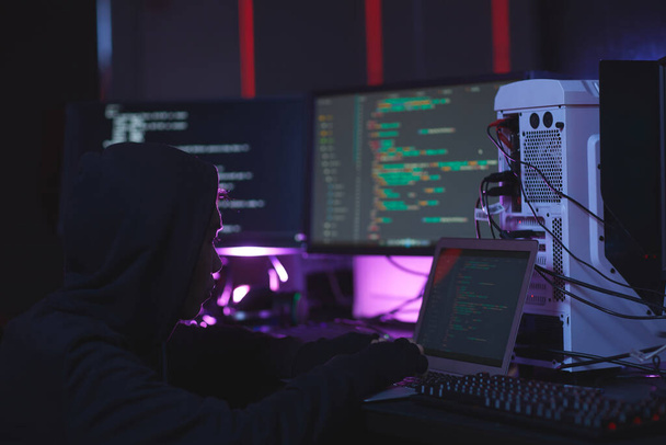 Porträt eines nicht wiedererkennbaren Hackers, der Computergeräte mit Programmiercode auf Bildschirmen im Darkroom benutzt, Cybersicherheitskonzept, Kopierraum - Foto, Bild